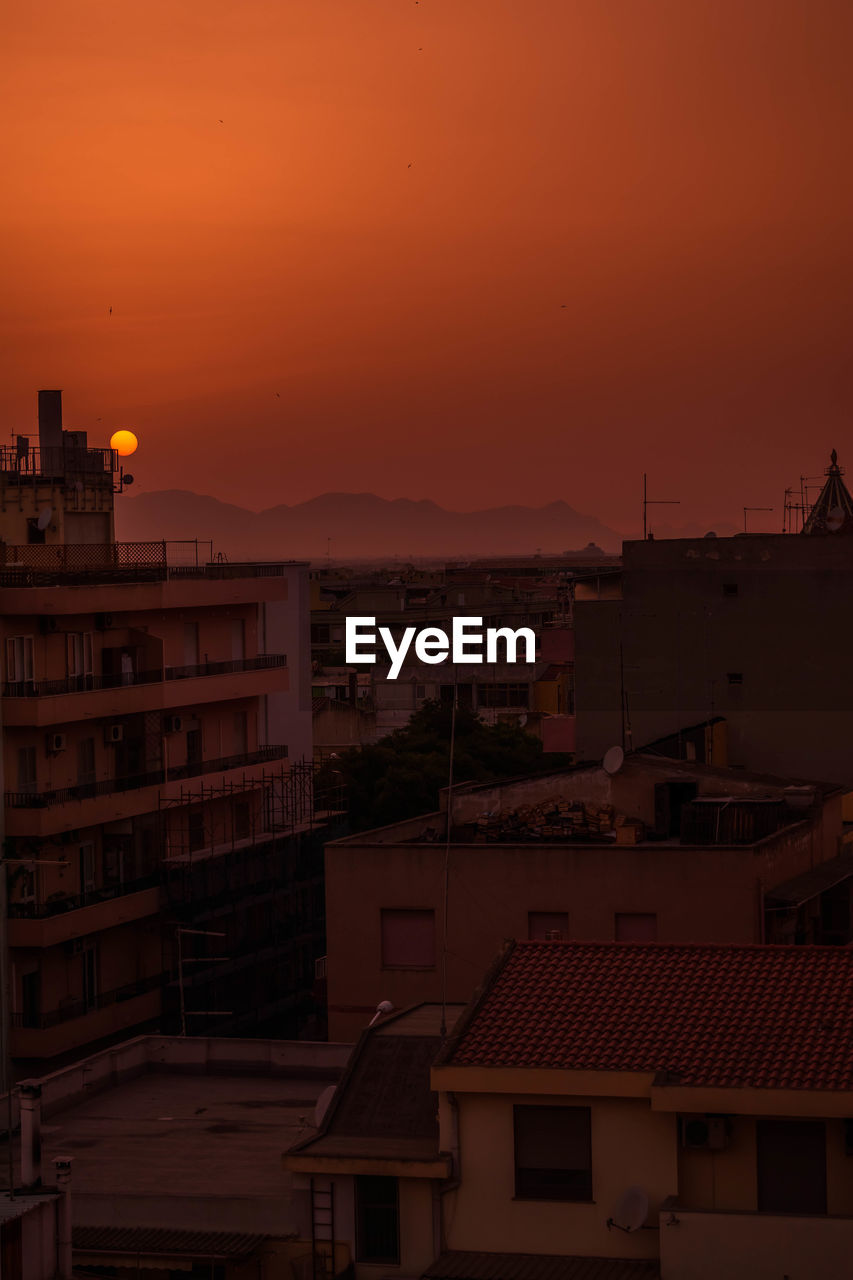 HIGH ANGLE VIEW OF BUILDINGS AGAINST ORANGE SKY