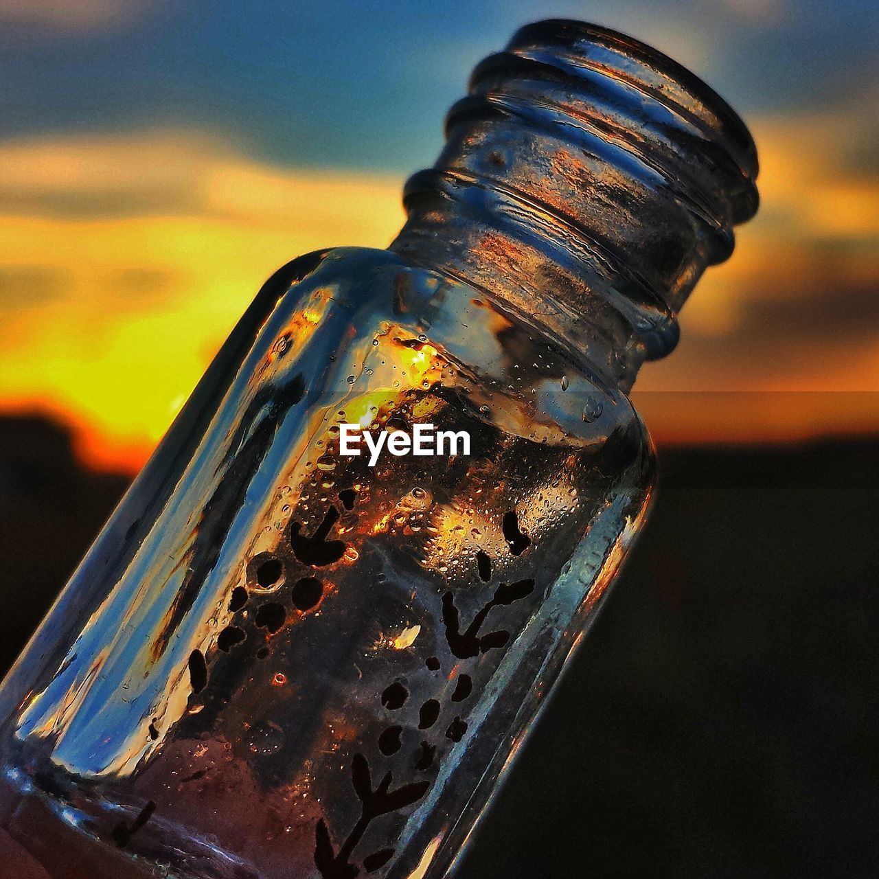 Glass bottle against sky at sunset