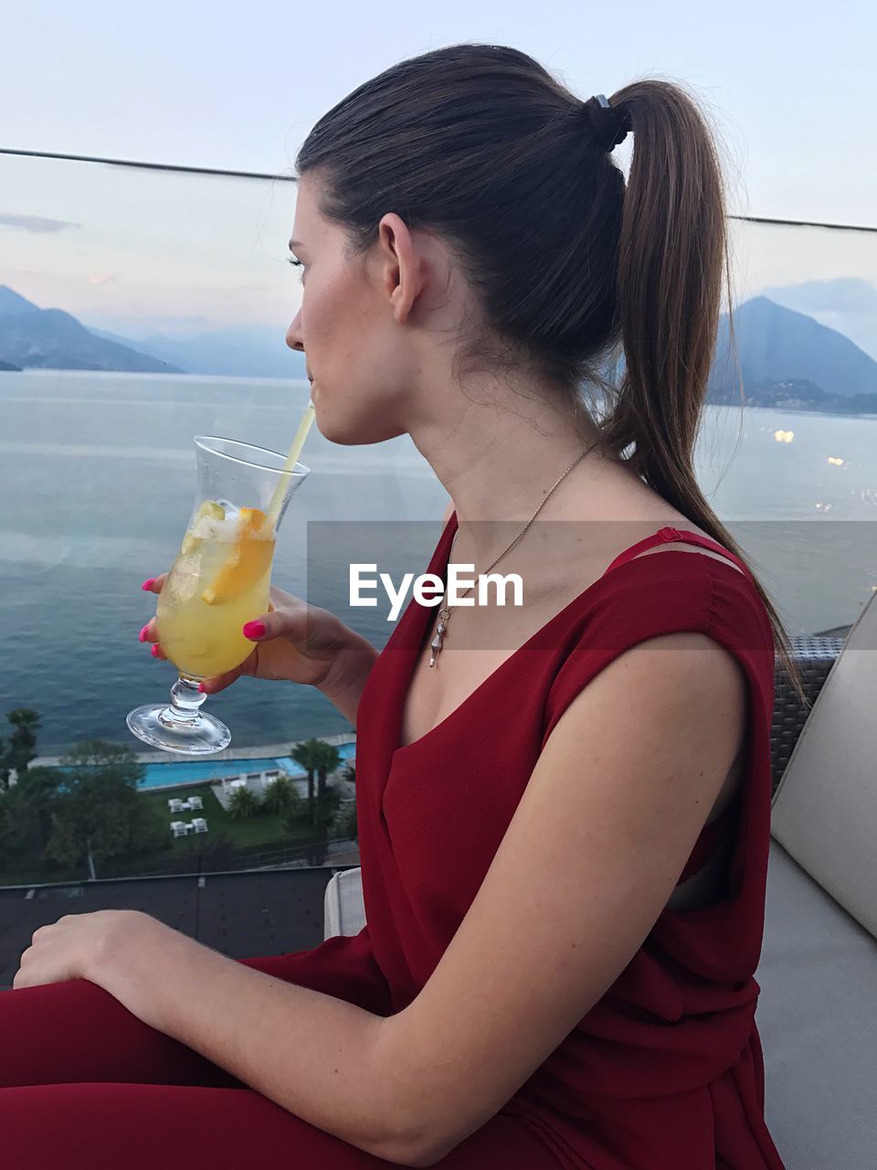 Young woman looking at sea while drinking juice during sunset