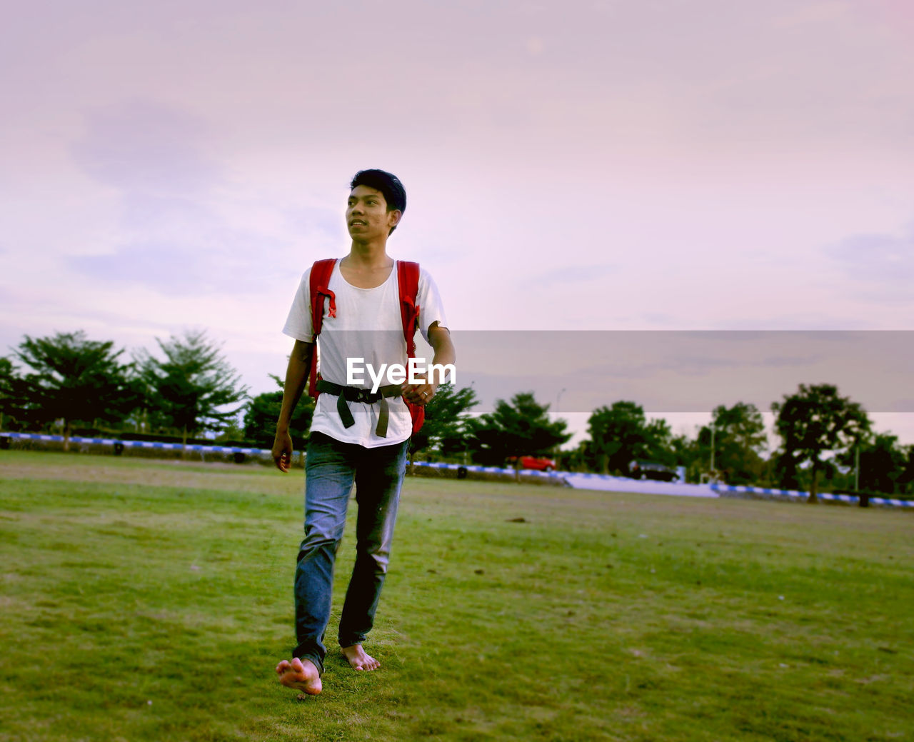 Thoughtful of young man walking on field against cloudy sky during sunset