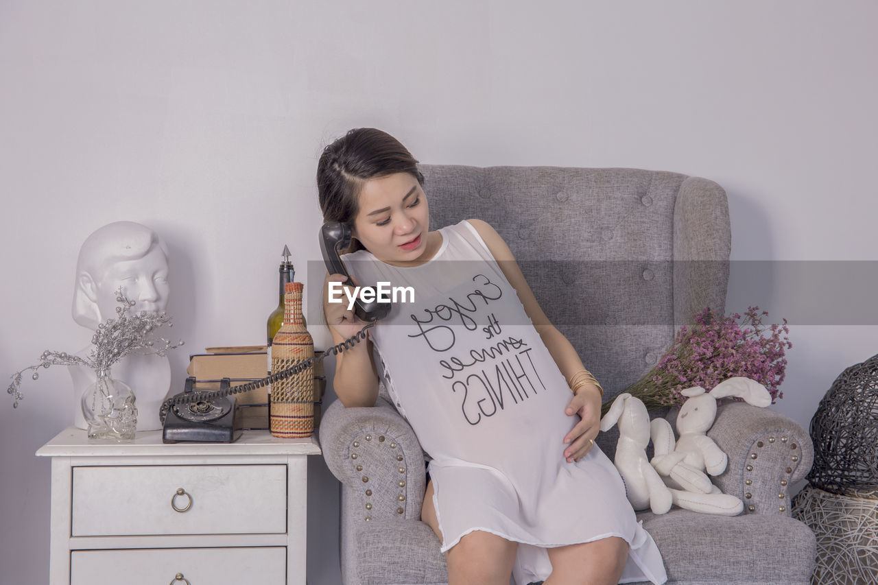 Pregnant woman talking on rotary phone while sitting at home