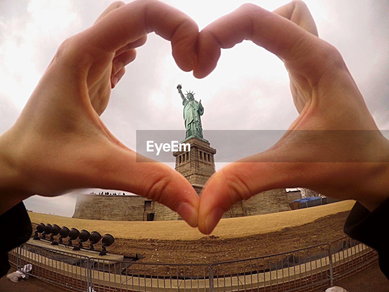 Cropped hand of woman making heart shape against historic statute