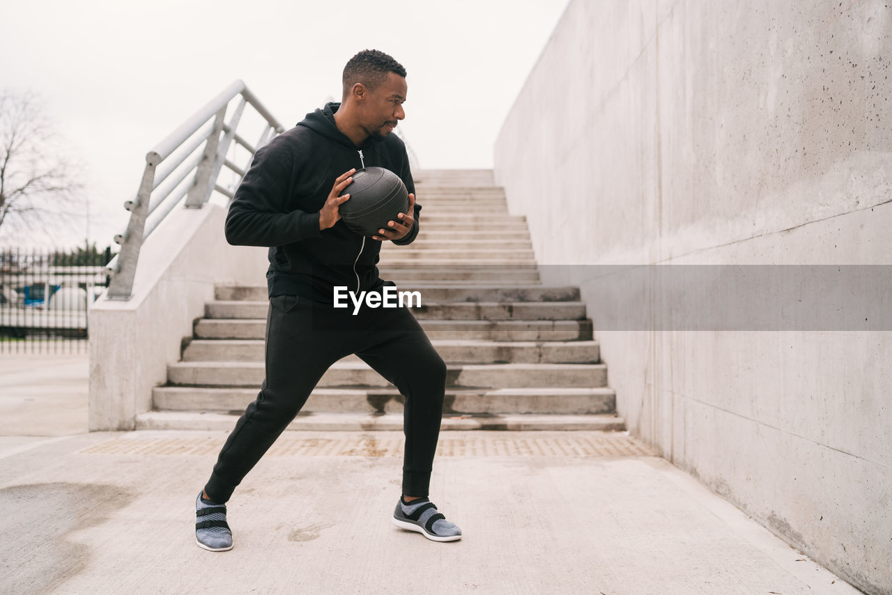 Full length of man exercising with medicine ball against wall