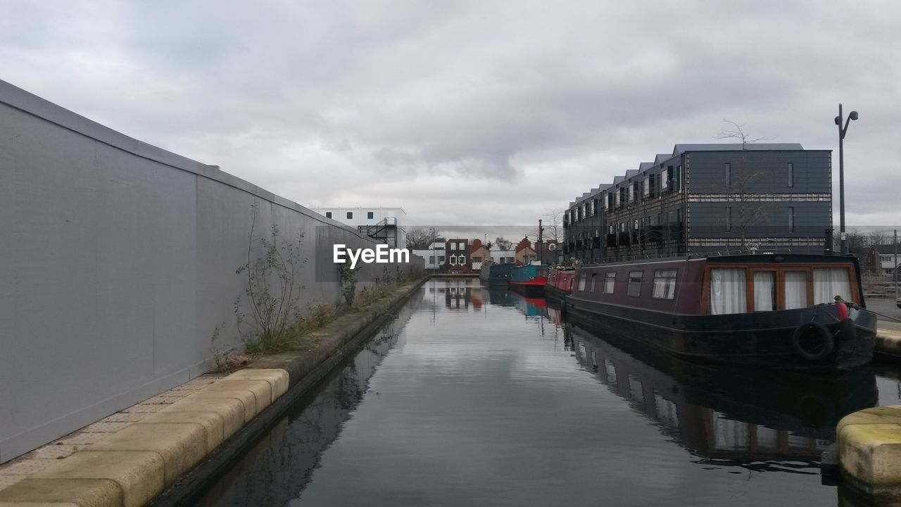 Boat moored on canal against cloudy sky