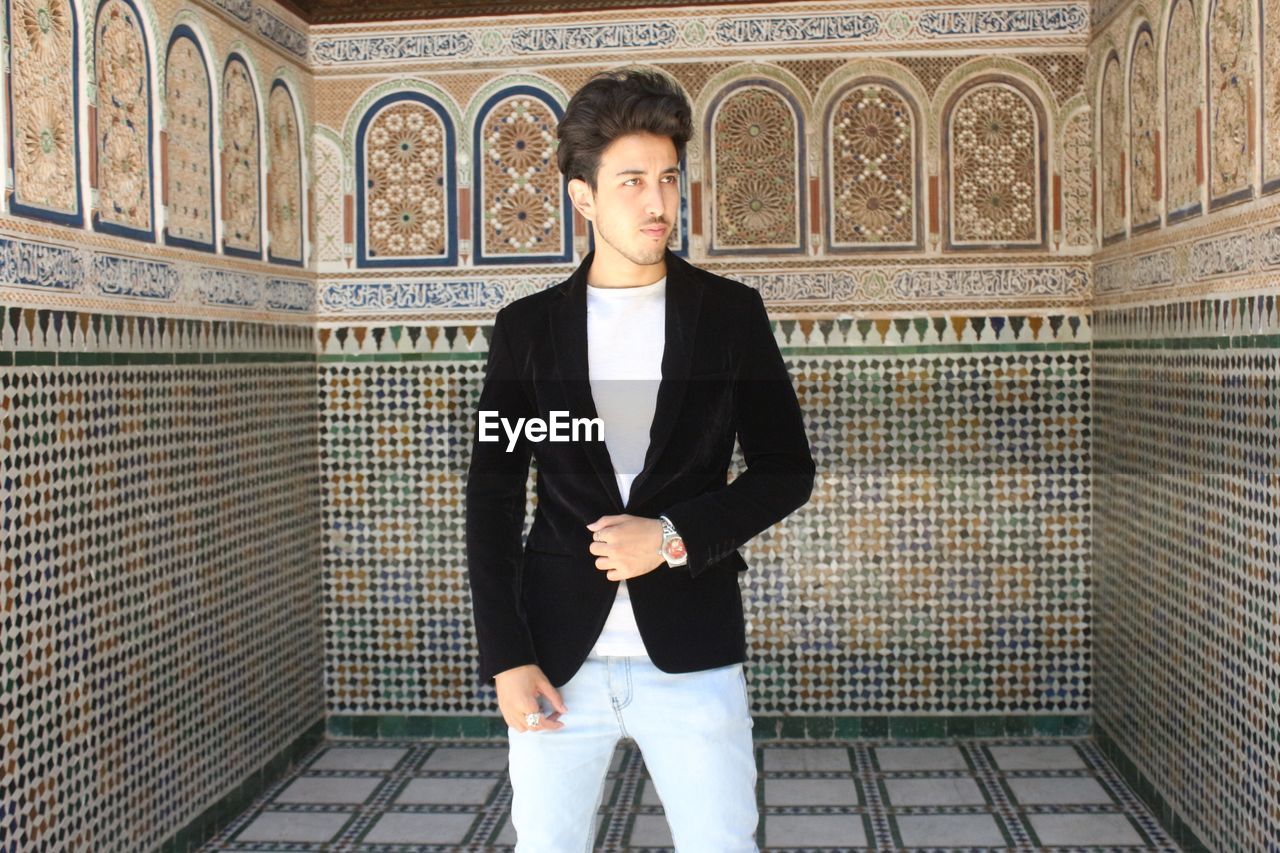 PORTRAIT OF A YOUNG MAN STANDING AGAINST WALL