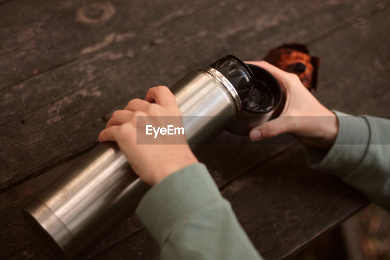 Woman pours tea from a thermos next to a muffin outdoors