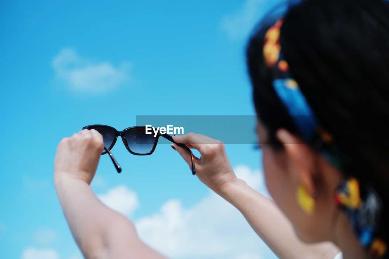 Low angle view of woman holding sunglasses against sky