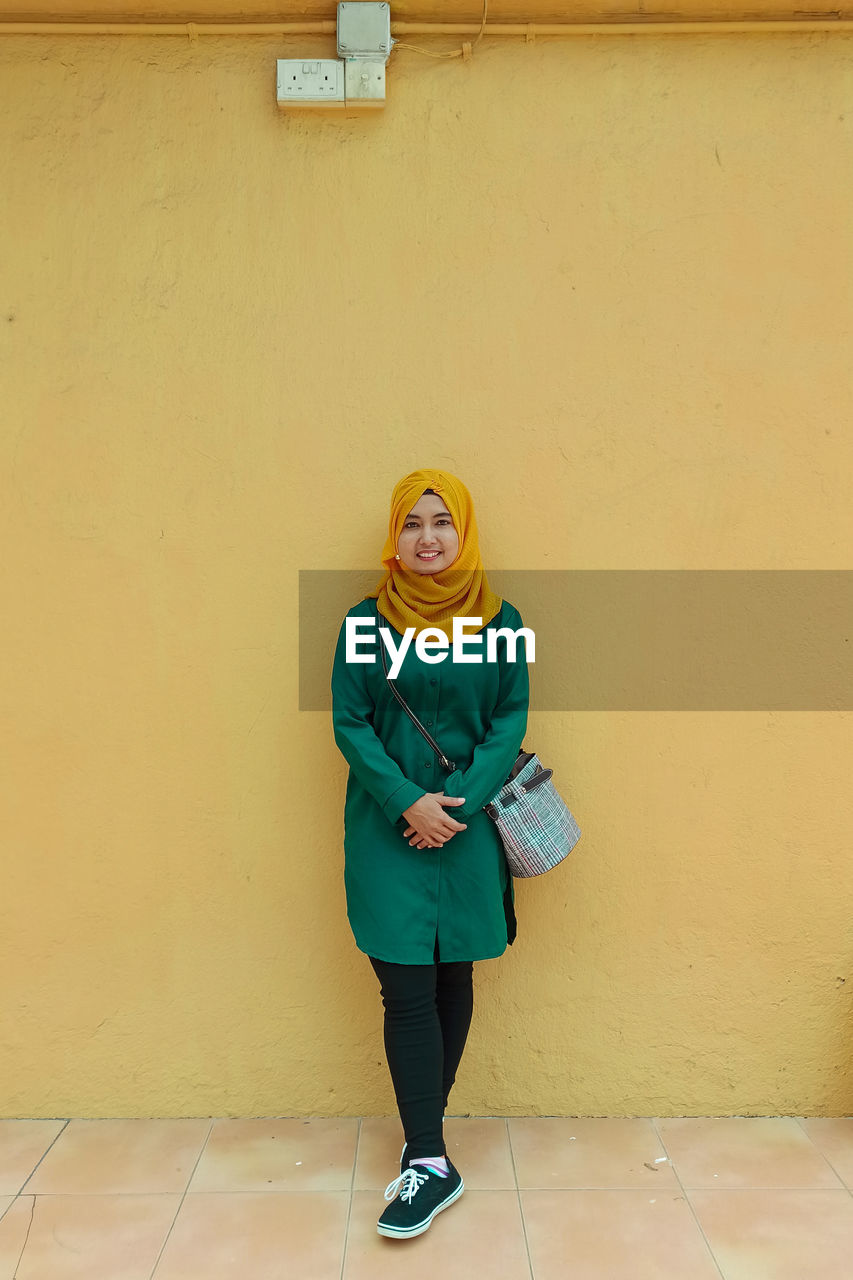 Portrait of smiling young woman standing against yellow wall