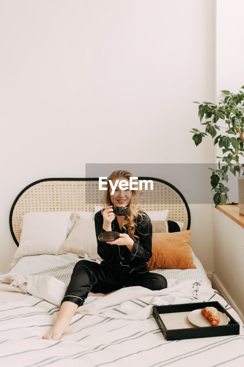 Beautiful happy smiling girl enjoying and having breakfast in bed in the morning in a cozy home