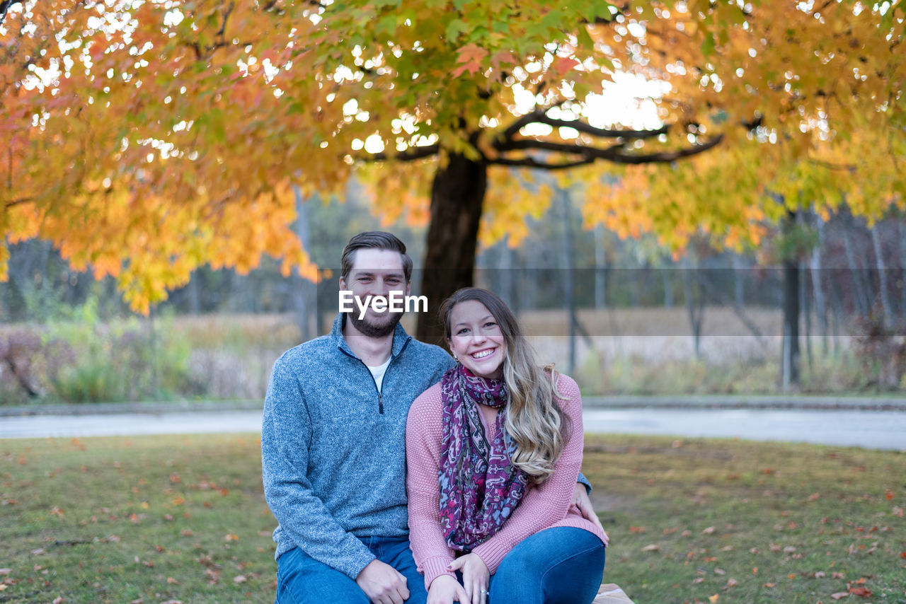 PORTRAIT OF A SMILING YOUNG WOMAN SITTING ON TREE