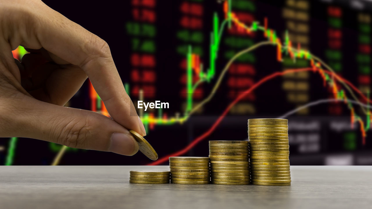 Cropped image of hand stacking coins on table against graph