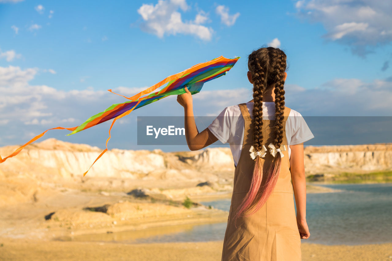 A teenage girl with a kite climbing to the top of the mountain looks into the distance.