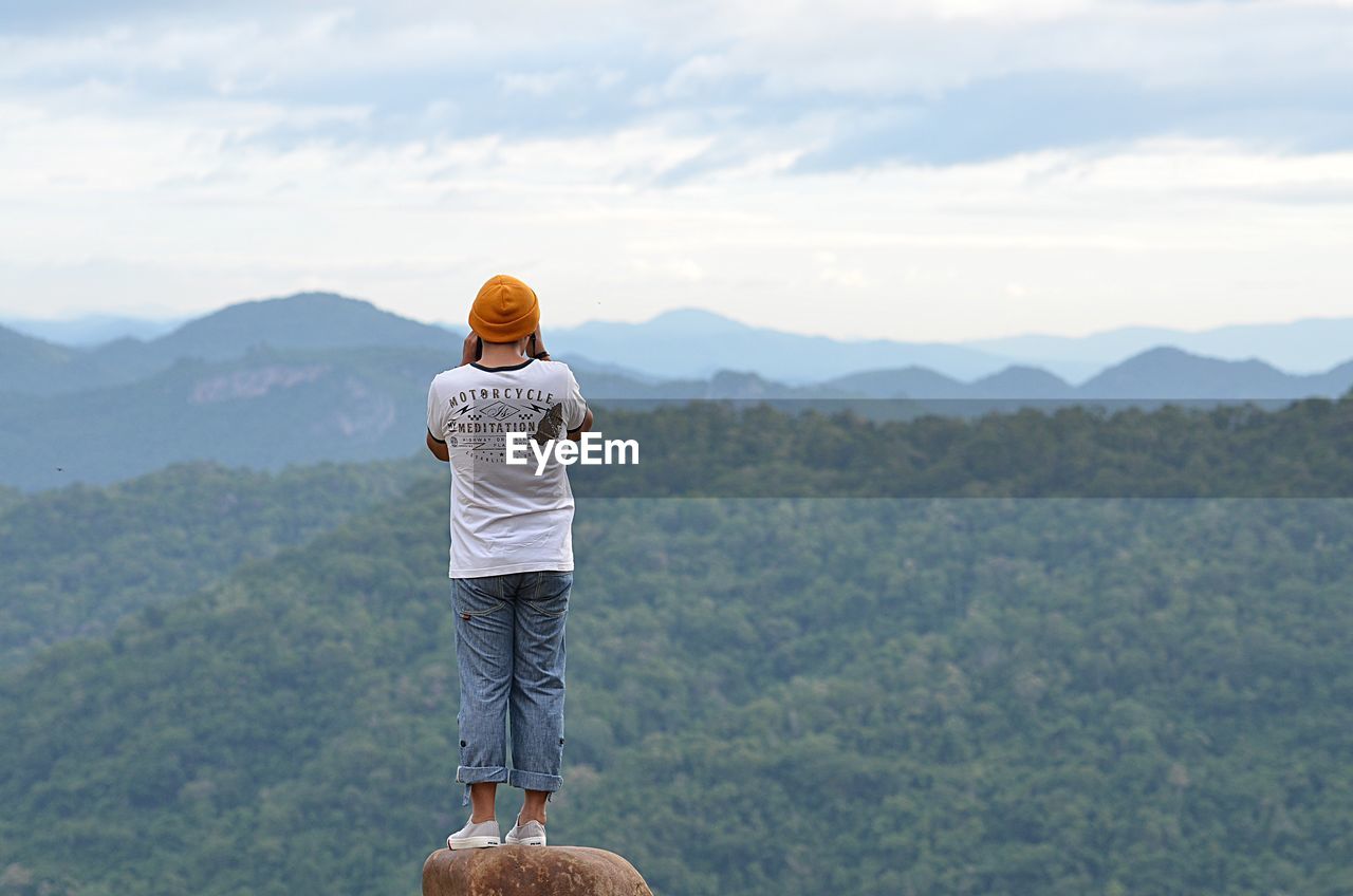 Rear view of man standing on mountain against sky