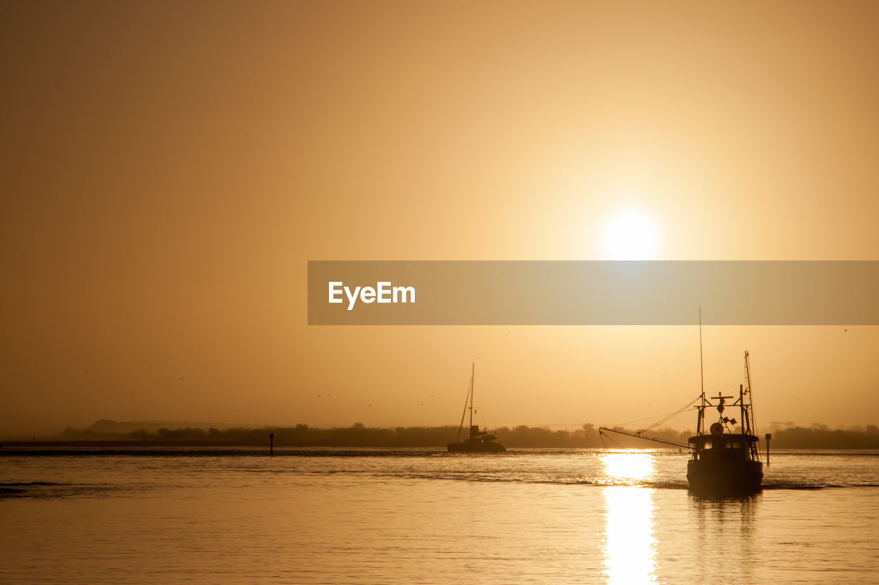 BOATS MOORED IN SEA AGAINST SKY DURING SUNSET