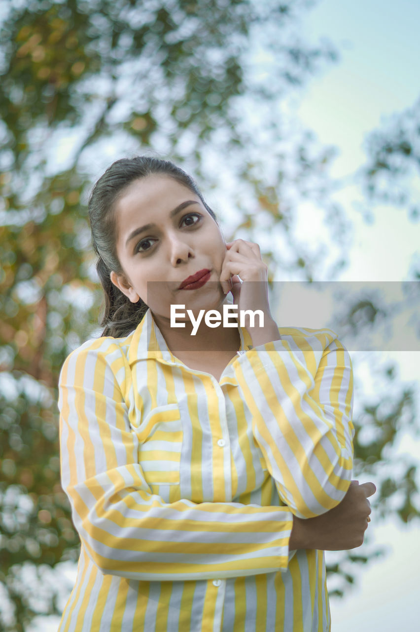 Portrait of smiling young woman standing against trees