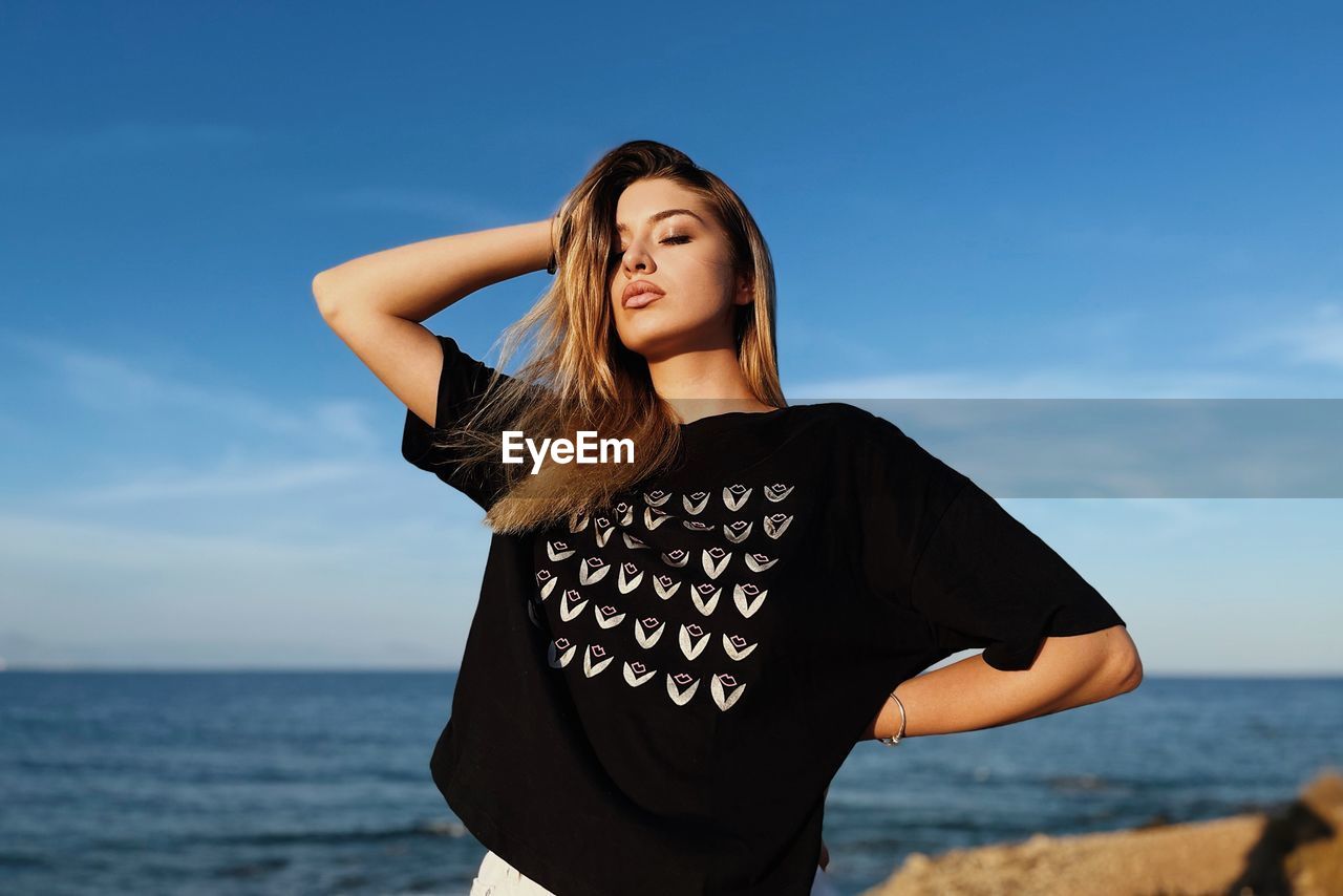 Young woman standing at beach against sky