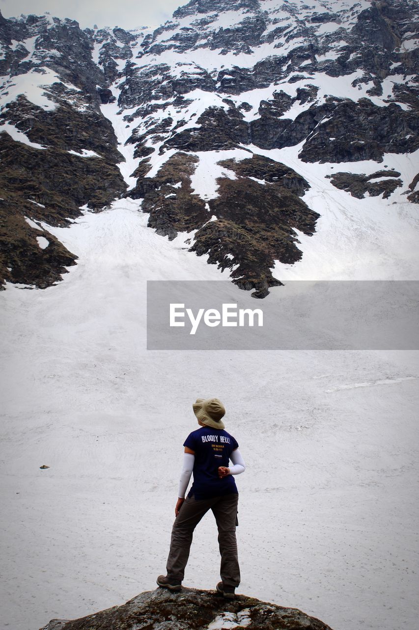 Full length of woman standing on rock against snowcapped mountain