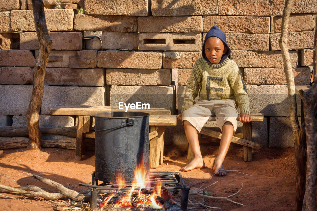 Portrait of boy sitting by campfire in village