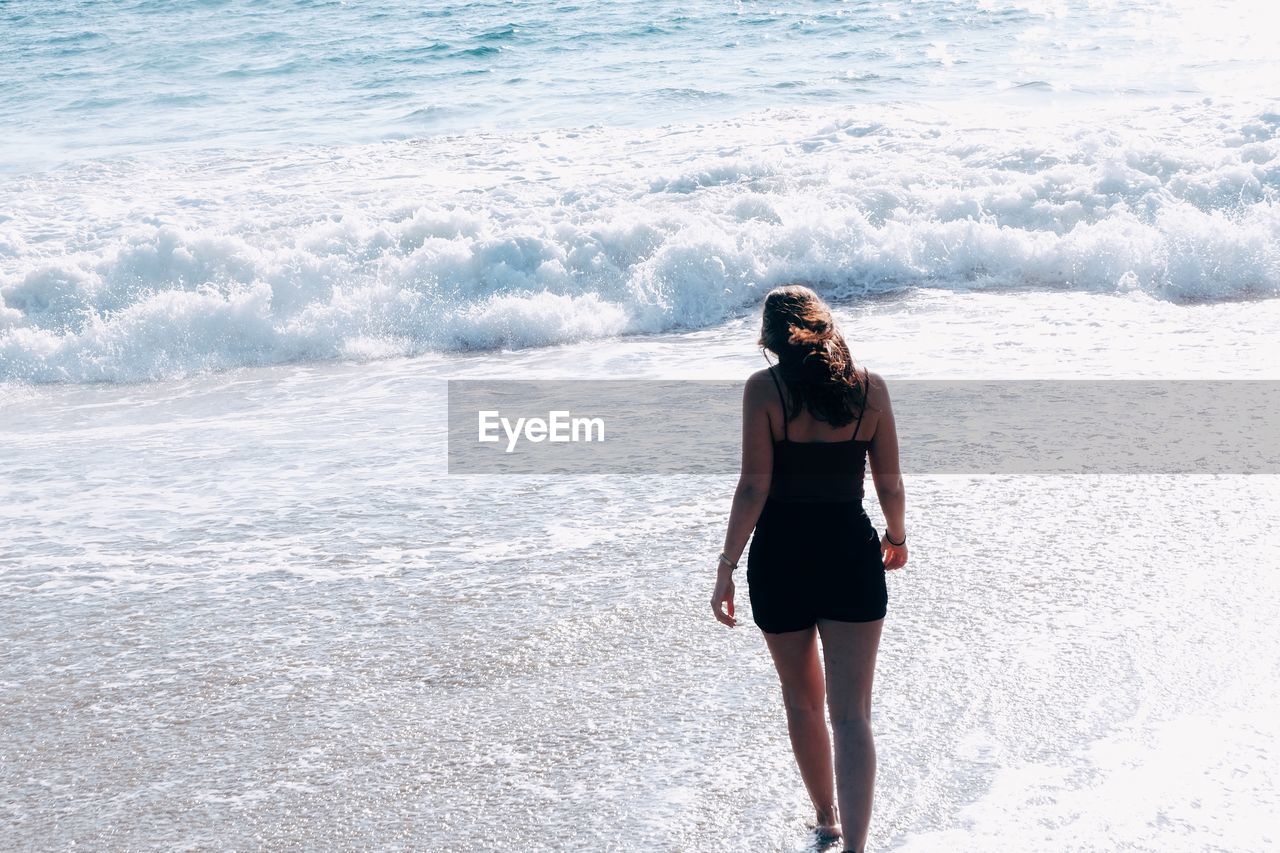 Rear view of young woman walking at beach on sunny day