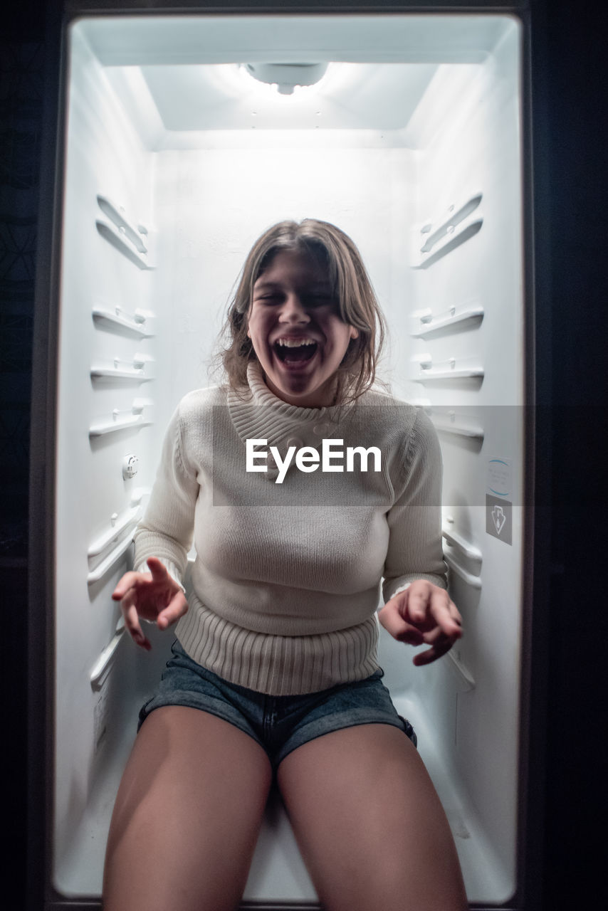 Portrait of smiling girl sitting in refrigerator