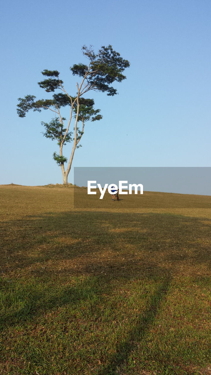 Man with bicycle on field against clear sky