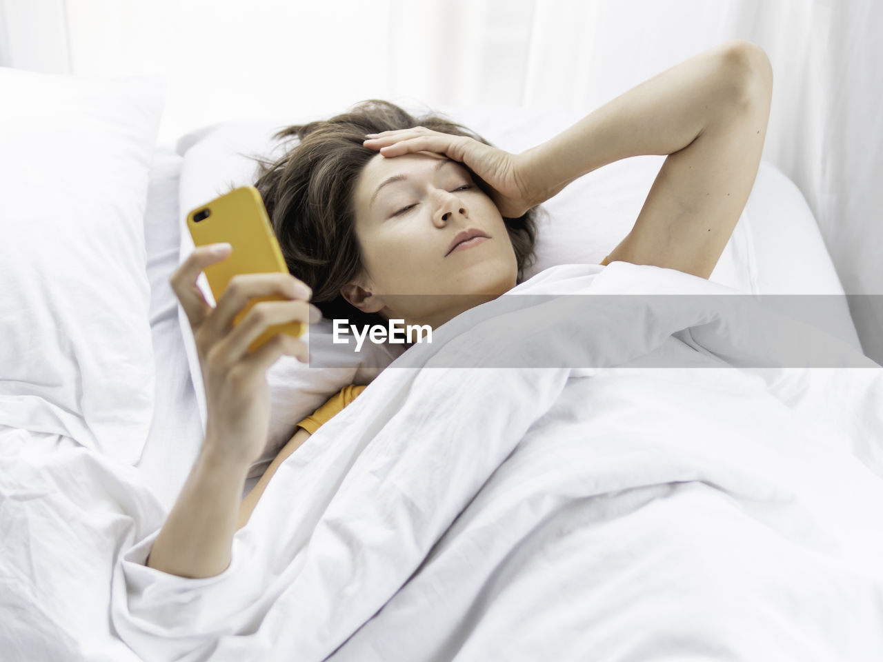 Woman holding mobile phone lying on bed at home