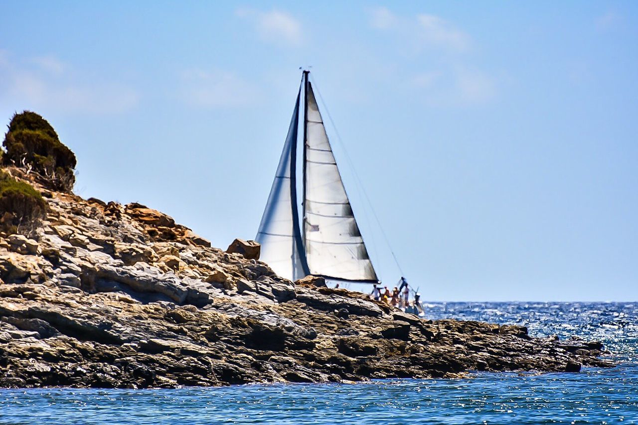 Sailboat by rock formation on sea against sky