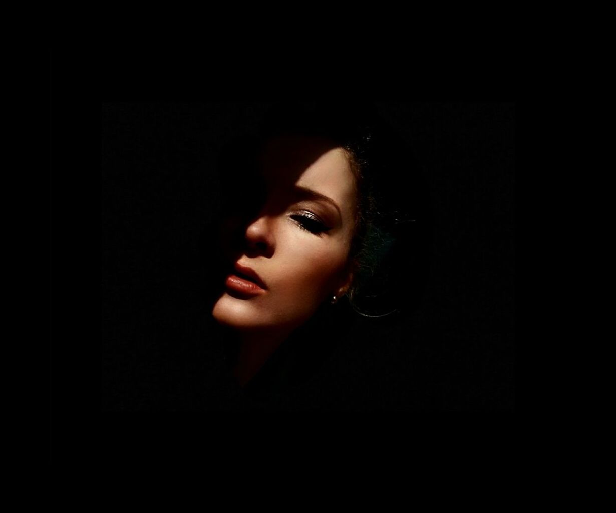 CLOSE-UP PORTRAIT OF YOUNG WOMAN IN DARK ROOM