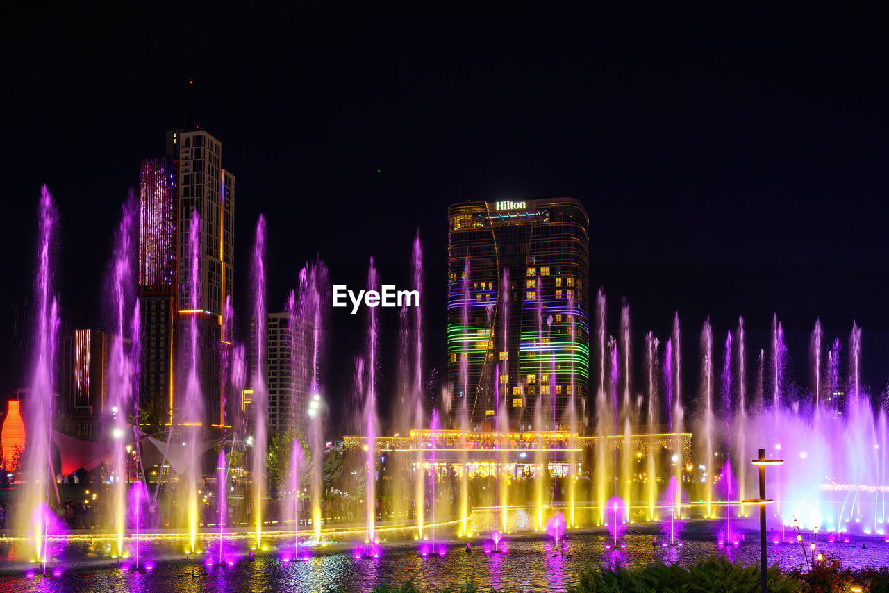 night, illuminated, architecture, fountain, water, no people, motion, nature, built structure, travel destinations, landmark, sky, building exterior, outdoors, celebration, purple, long exposure, water feature, arts culture and entertainment, city, multi colored, travel, skyline, event