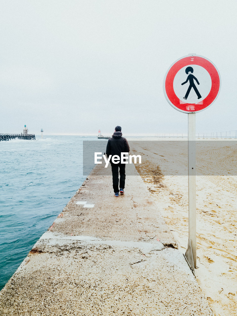 Rear view of man standing on beach with forbidden signal