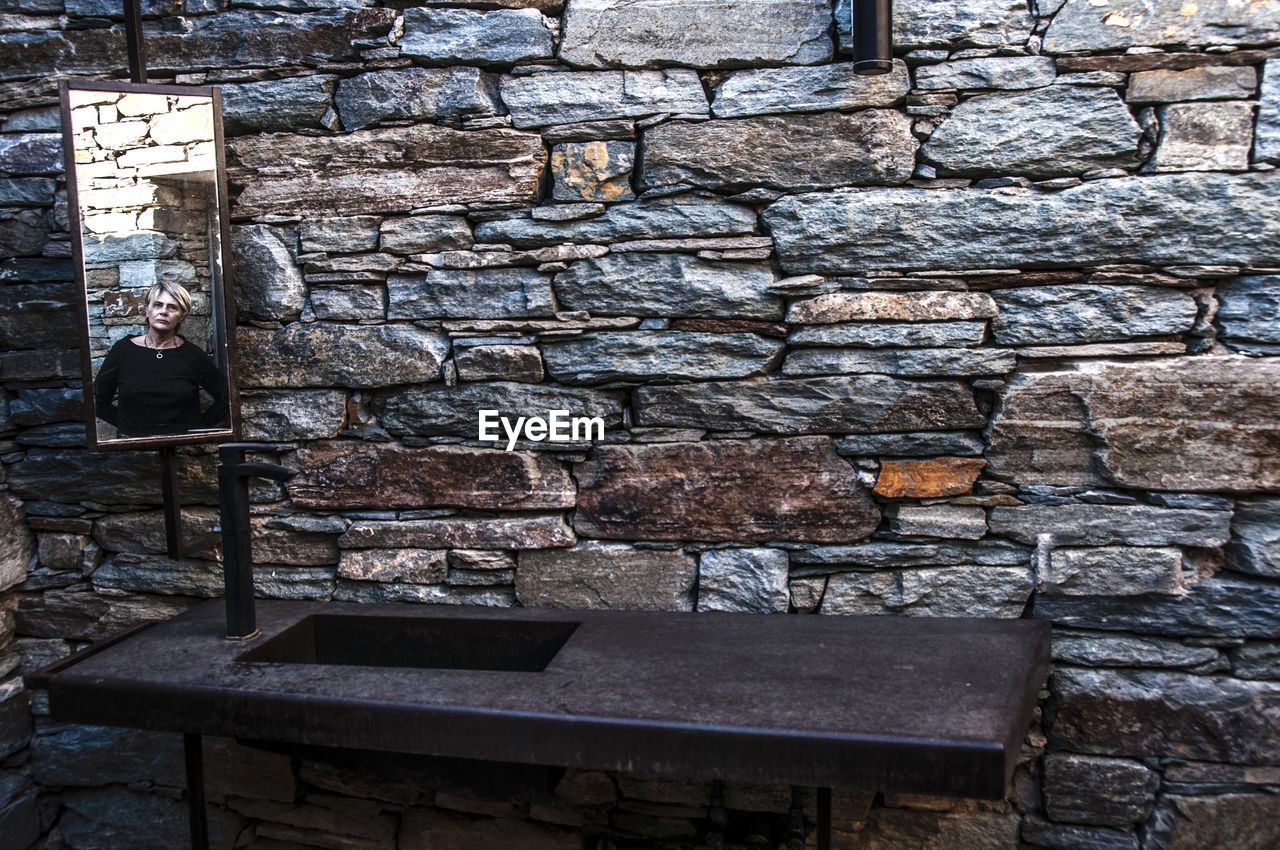 Reflection of woman seen in mirror against stone wall