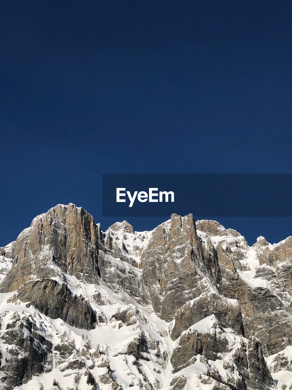 Low angle view of snowcapped mountains against clear blue sky