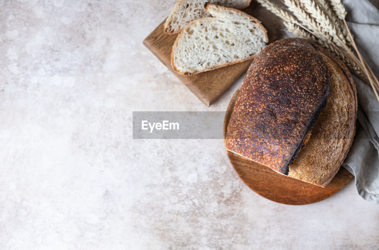 Loaf of fresh homemade sourdough bread on wooden plate with wheat ears.