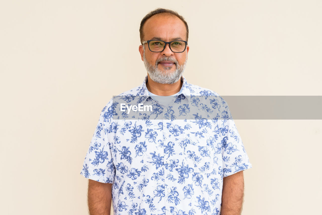 PORTRAIT OF MATURE MAN STANDING AGAINST GRAY BACKGROUND