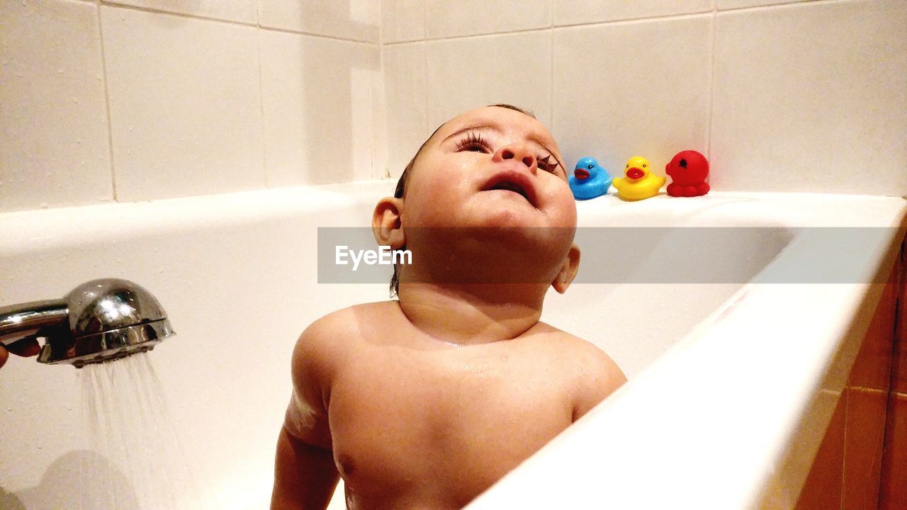 Shirtless baby boy sitting in bathtub at bathroom