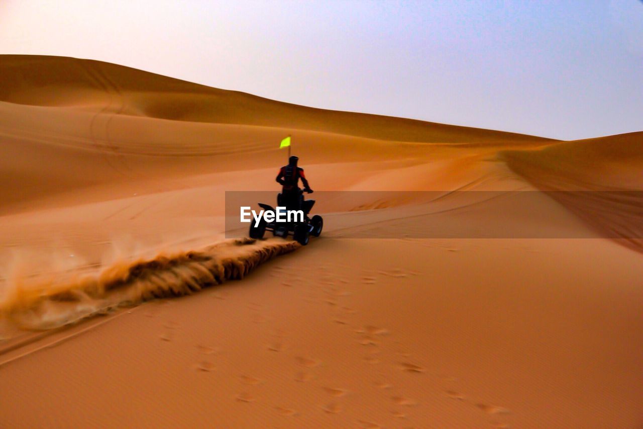 Rear view of man riding quadbike on sand at desert