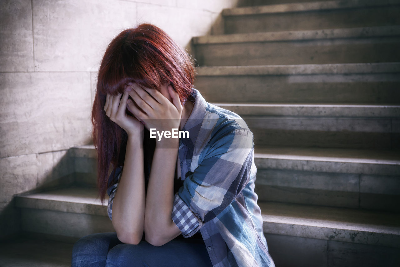 Depressed girl covering face with hands and sitting on steps