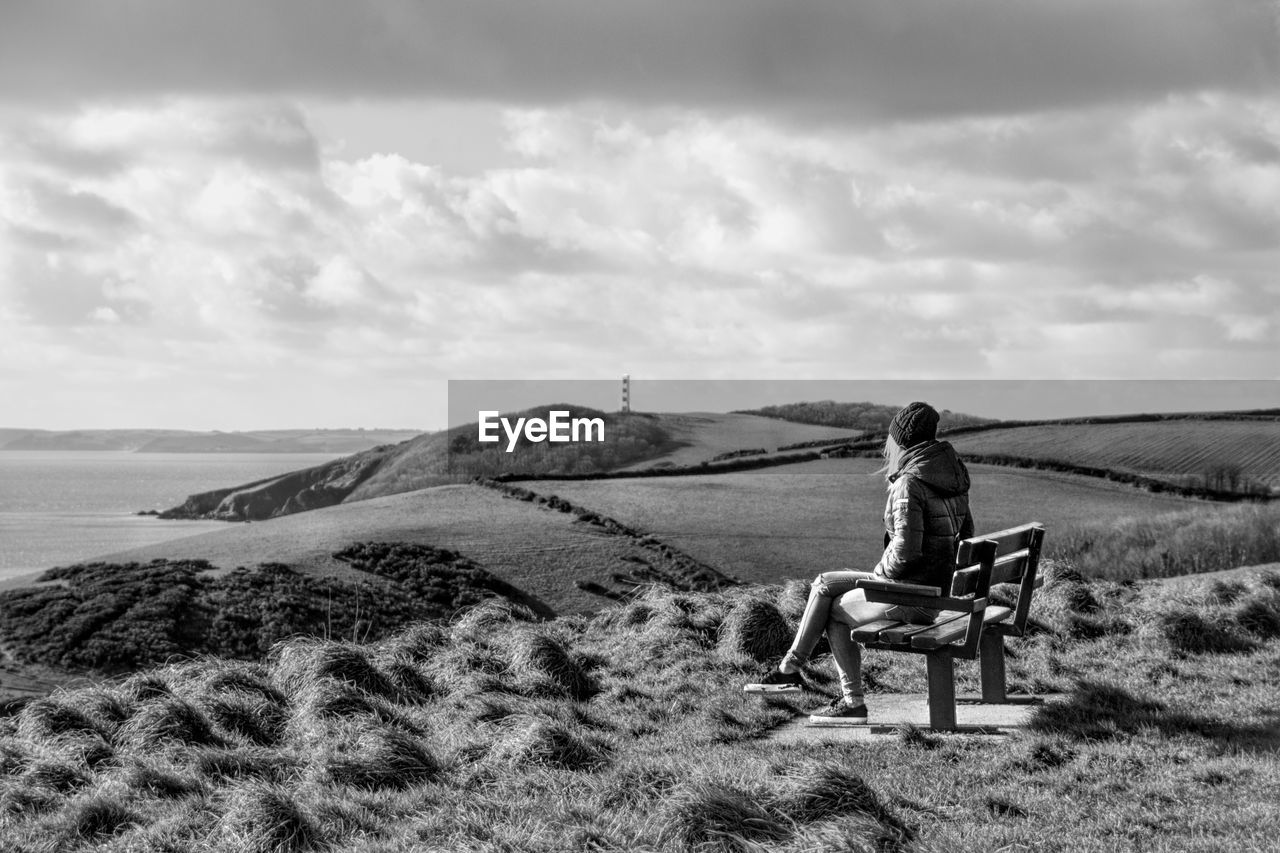 Woman sitting on bench while looking at sea