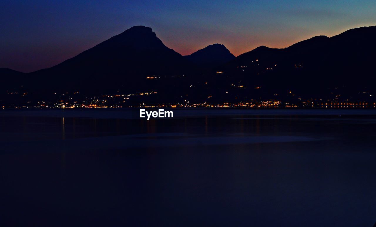 ILLUMINATED CITY BY SILHOUETTE MOUNTAIN AGAINST SKY