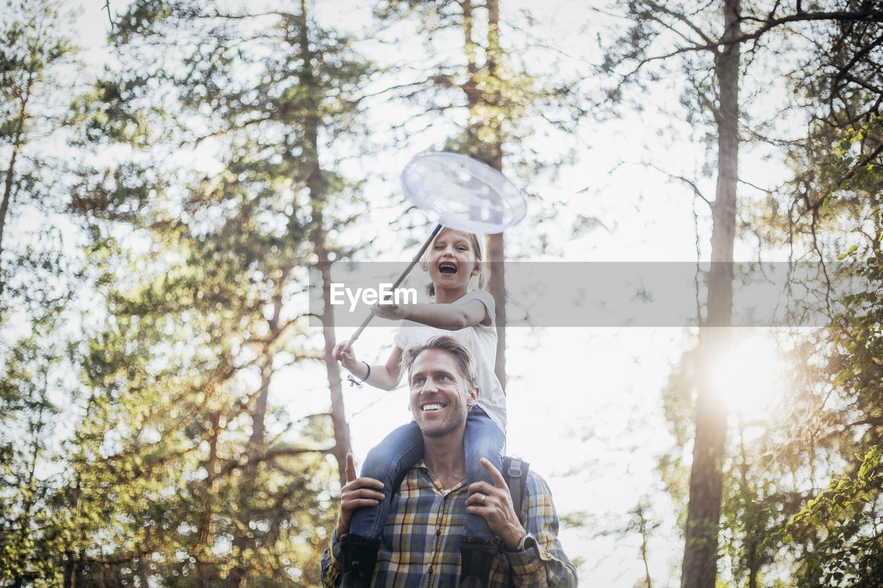 Smiling father carrying happy daughter on shoulder while walking in forest
