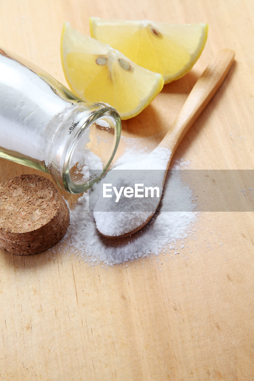 Close-up of powdered sugar in wooden spoon with lemon slices on table