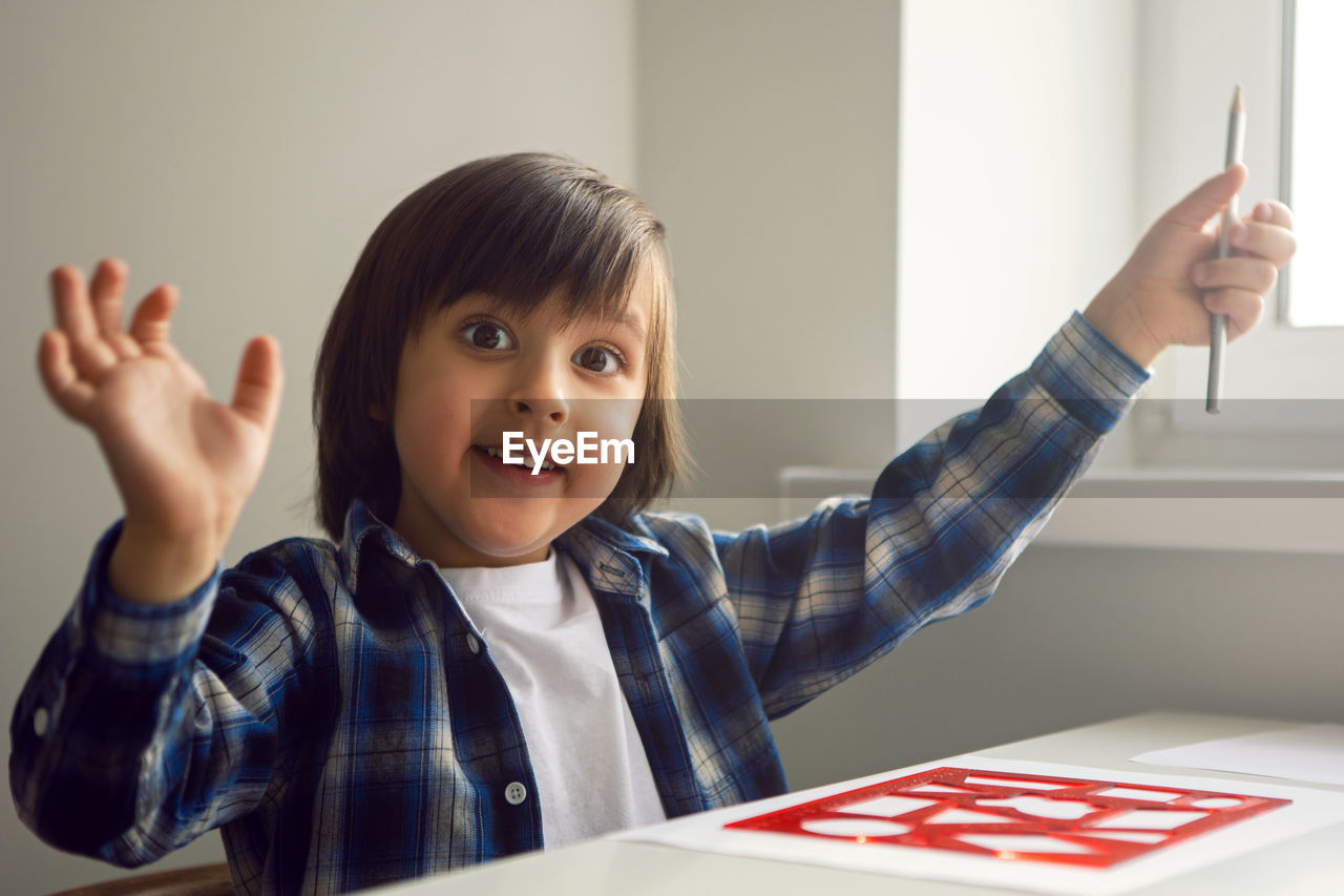 Boy child draws on paper with a ruler on a table sitting by the window