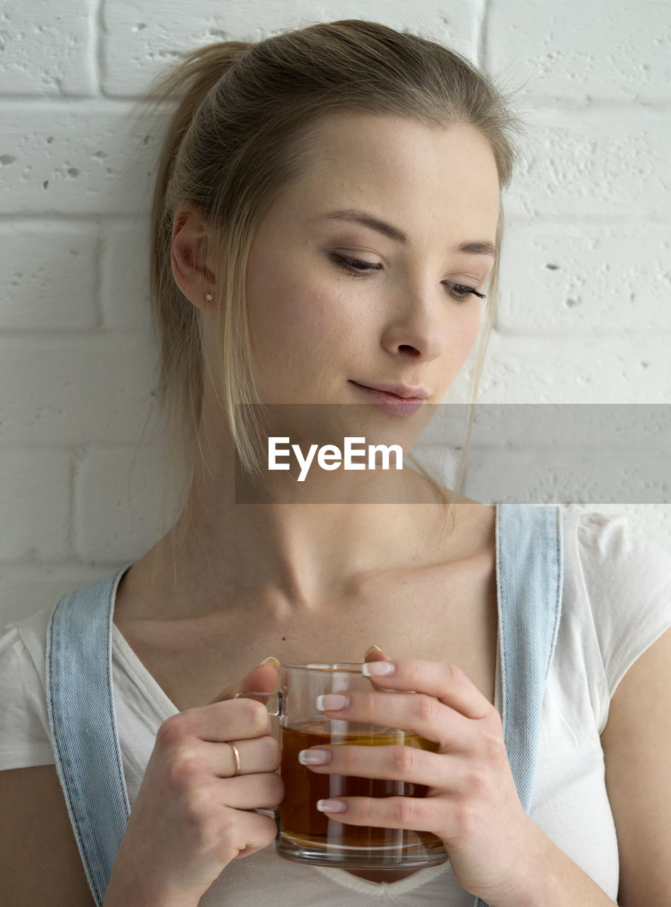 Young woman holding drink while standing against wall