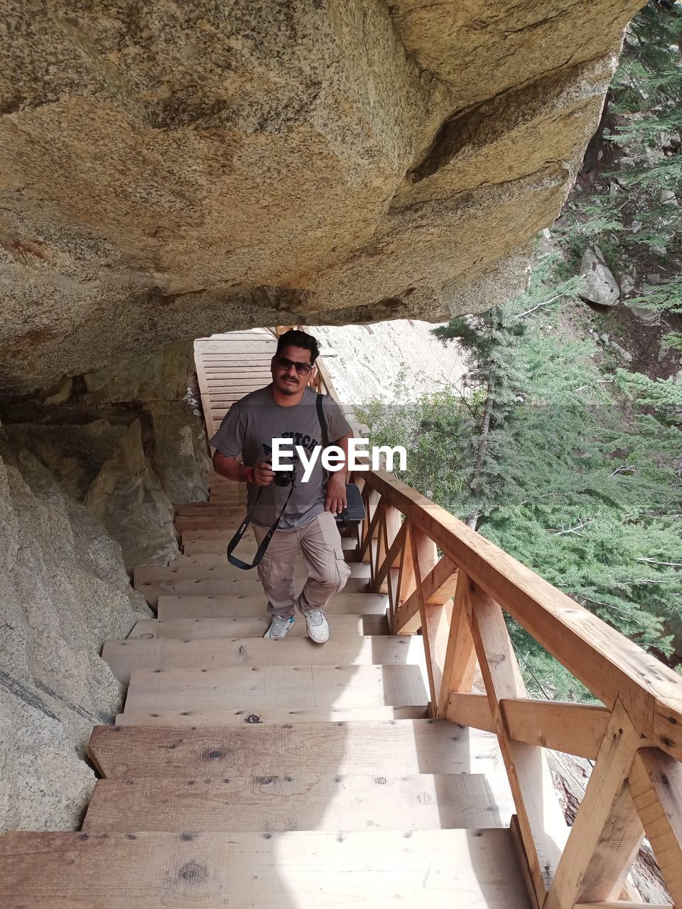 full length, one person, leisure activity, adult, nature, lifestyles, architecture, men, front view, casual clothing, day, young adult, rock, staircase, cave, standing, outdoors, railing, travel, sunlight, high angle view, wood, sunglasses, looking at camera, built structure, adventure, portrait, rock formation, activity, women, bridge, glasses, vacation, wadi, land, trip, smiling, steps and staircases, holiday, person, walking, fashion