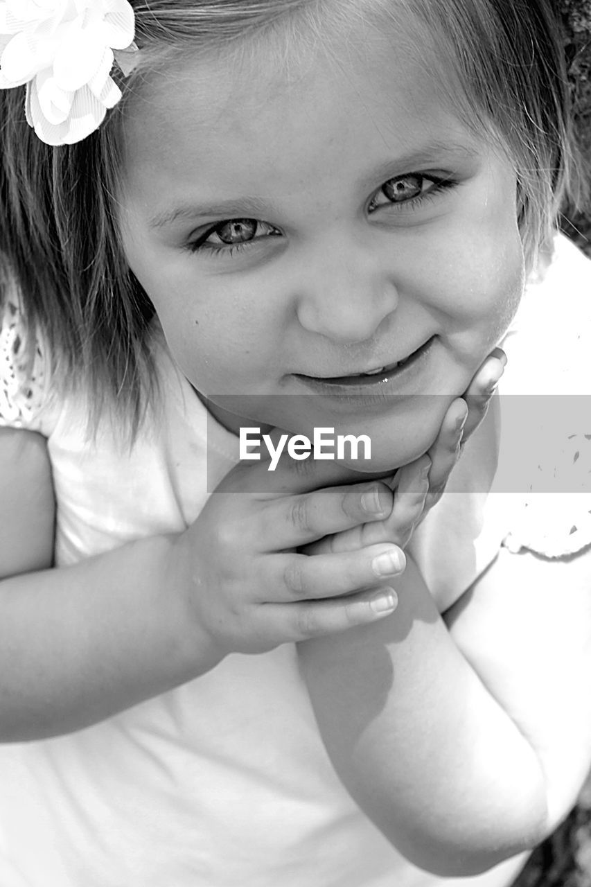 High angle close-up portrait of smiling girl with hand on chin