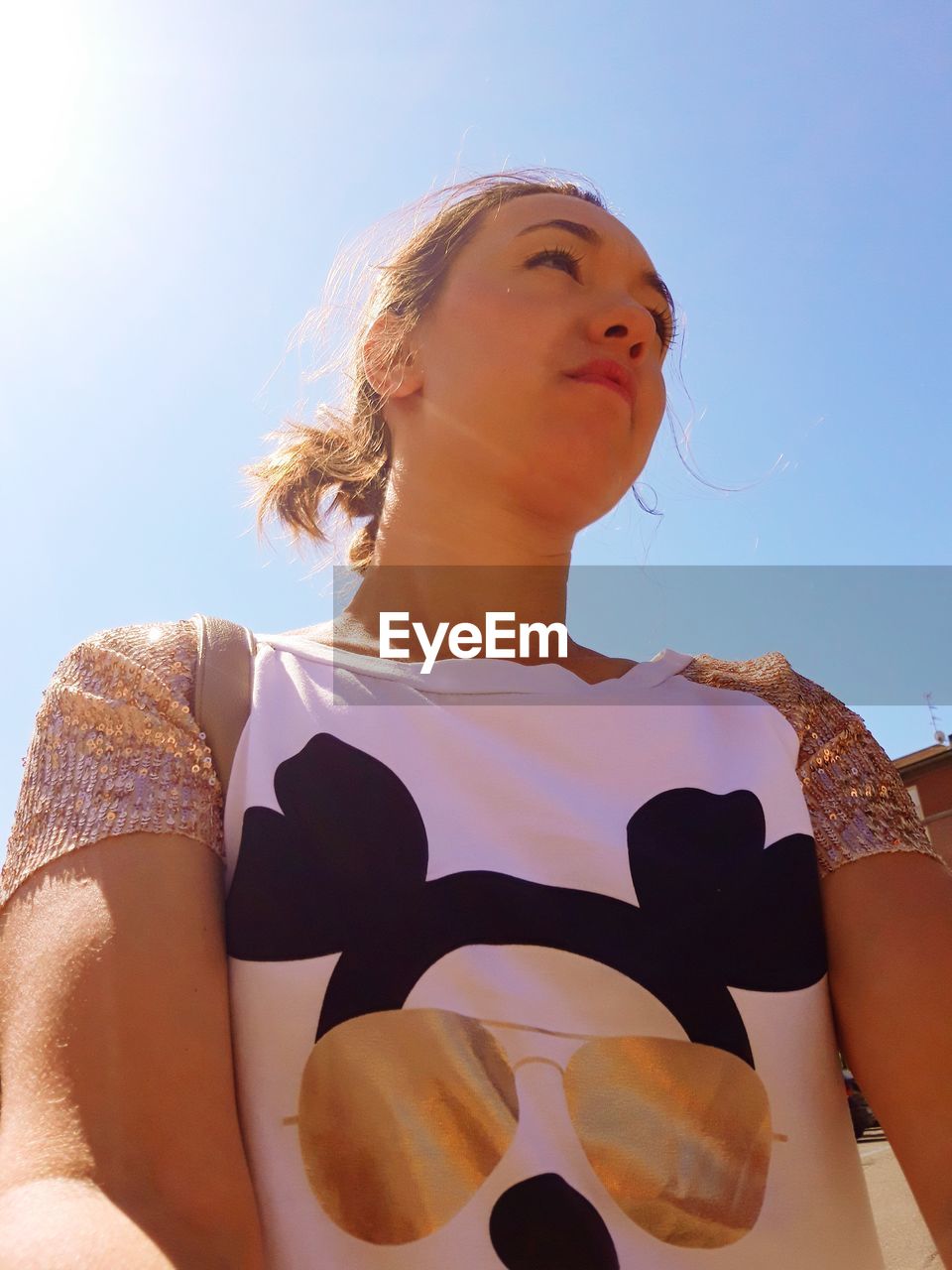 LOW ANGLE VIEW OF WOMAN LOOKING AT CAMERA AGAINST SKY