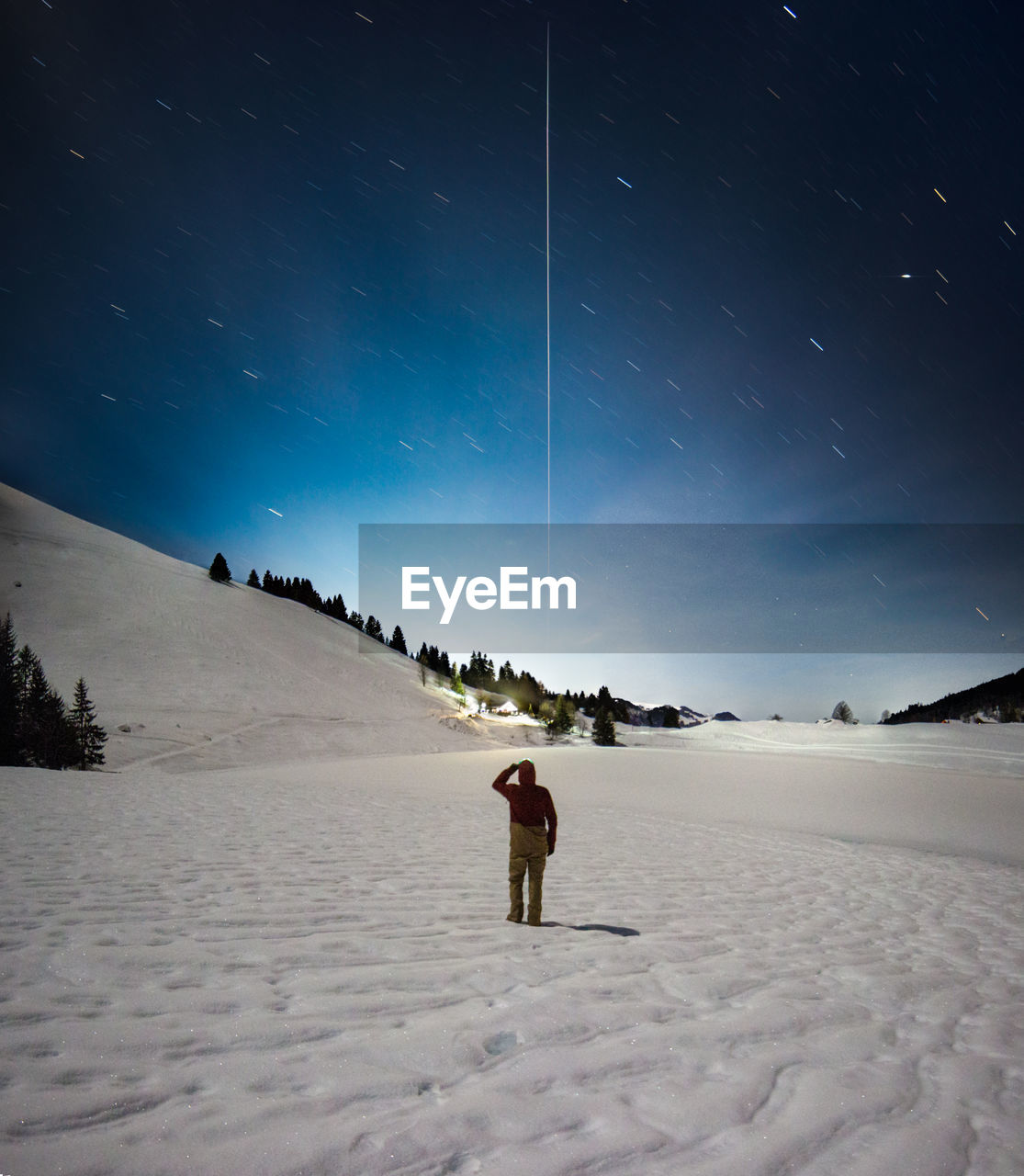 Full length of person standing on snow covered land against star trails at night