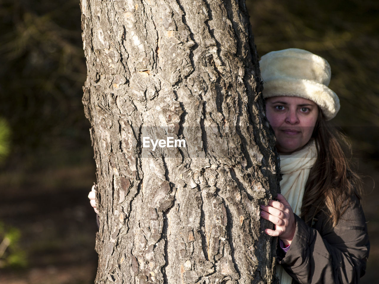 Portrait of mature woman standing behind tree trunk