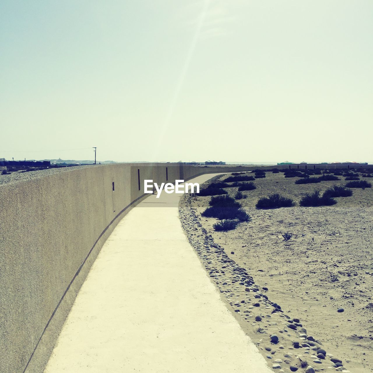 Walkway by retaining wall on beach against sky