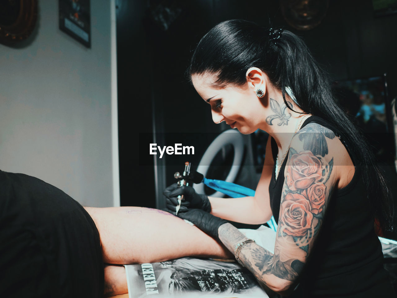 Young woman tattooing statue of liberty man on calf at parlor